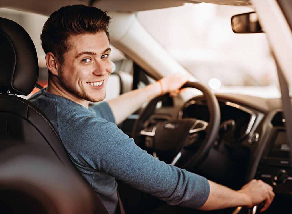 young man about to drive, smiling because he knows he has auto insurance logan county il